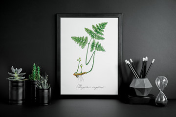 Black desk with mock up photo frame, pencils and plants.