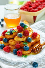 Traditional Breakfast - French toast with honey and fresh berries - raspberries and blueberries in a white plate on the table