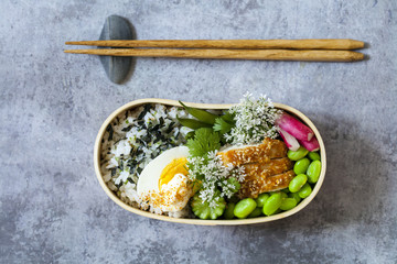 Japanese bento lunch box with sesame crusted chicken, edamame beans, egg and spicy rice