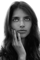 Portrait of a young girl with long hair softly touching her face with one hand and looking upwards, black and white