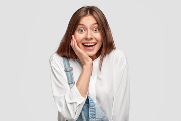 Delighted hilarious teenager looks positively at camera, recieves good news from friend, wears...