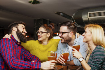 Four friends toasting with full glass of bear in pub and smile