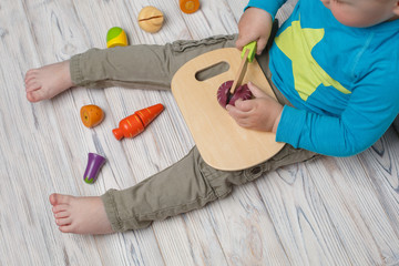 child plays in the chef close up portrait. toy wooden vegetables in baby hands on background top view. baby boy slicing and cut toy vegetables. interesting developing game.