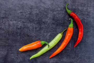 Different colors of hot chili pepper on dark stone background. Concept- hot news, spices, recipes,...