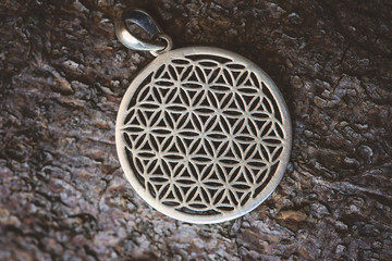 Sacred geometry flower of life silver pendant on wooden background