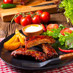 bbq spareribs on the plate with green salad and white sauce.