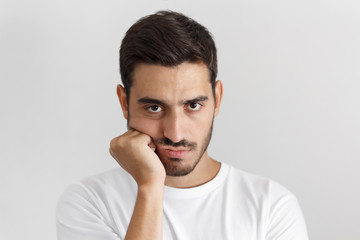 Close up portrait of bored young man in white tshirt with head on chin isolated on gray background
