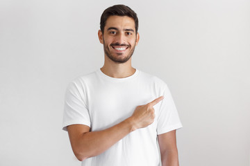 Handsome young man in white t-shirt pointing right with his finger isolated on gray background
