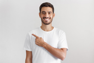 Handsome man in white t-shirt pointing left with finger isolated on gray background