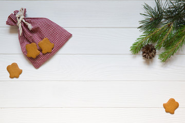 Christmas conceptual background, red and white chequered bag, ginger bells cookies, pinecone on white wooden background. Copy space, top view.