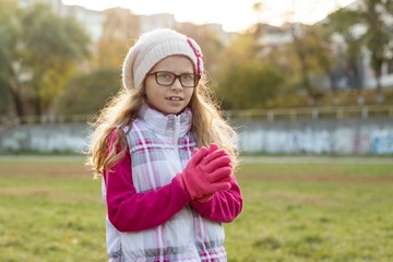 Portrait of a happy girl 7 years old, in a knitted hat, glasses, autumn sunny background