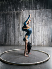 Young female acrobat standing on hand over gray background in photo studio