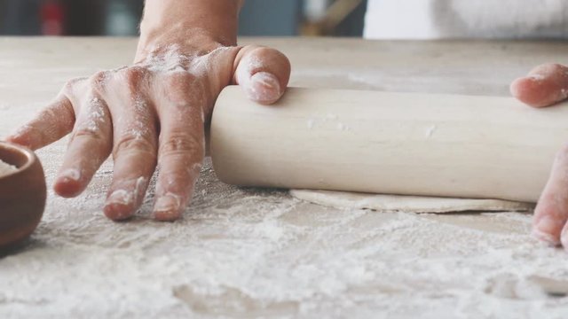 Female hands rolling dough on wooden table