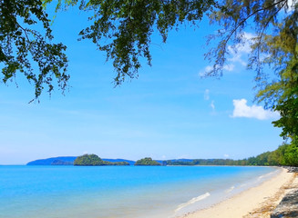 The beach of Southern Thailand. Small wave hit the shore. The sea is blue and the sky is clear, so you can see the small islands off the coast.