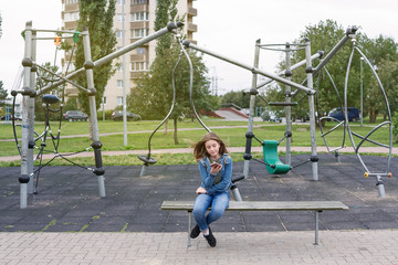 teenager girl is surfing internet with iphone mobile phone sitting on the playground in the town city