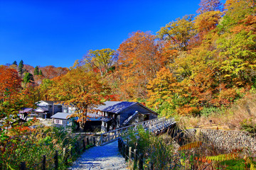 Rustic ryokan Magoroku Onsen among colorful autumn forest with blue sky in hot spring resorts of Nyuto Onsenkyo, Akita Prefecture, Japan