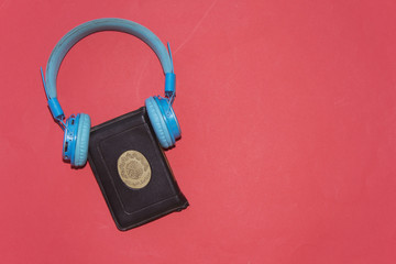 listen to quran concept, holy muslim book and bluetooth headphone  isolated on red background