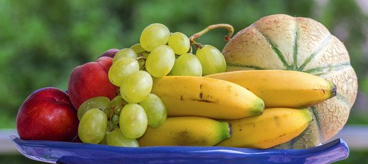 Set of fruit, melon, bananas, grapes and peaches, on a tray with green background