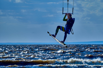 A male kiteboarder jumps above the surface of the water of a large river.  Splashes of water scatter in different directions.