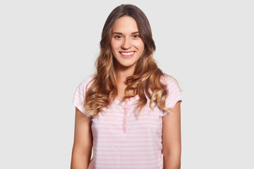 Fototapeta premium Lovely merry beautiful young Caucasian female in casual pyjamas, being in good mood ater good sleep, isolated over white background, shows perfect teeth, healthy skin, enjoys domestic atmopshere