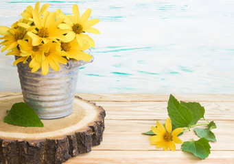 yellow daisies in a metal bucket close-up on a round slice of a tree. Rustic wooden table background.