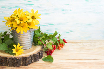 yellow daisies in a metal bucket and viburnum on a branch close-up on a round cut tree. Rustic wooden table background.