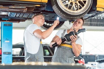 Two skilled auto mechanics analyzing together the rims of a lifted car while working in a modern...