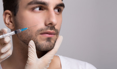 Handsome man receiving injection in his face - obrazy, fototapety, plakaty
