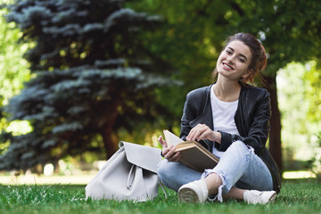 Happy woman sitting on grass and reading book