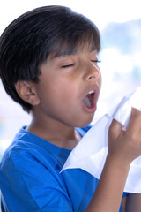 Child sneezing holding tissue in hands. Kid about to sneeze into napkin.