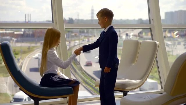 little boy is wearing suit is approaching to pretty little girl and shaking her hand