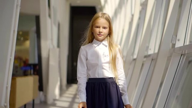 pretty little girl is wearing white shirt and black skirt is walking in space of modern school in sunny day