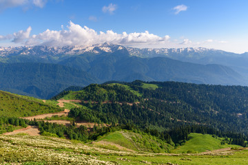 Naklejka na ściany i meble Beautiful view of the mountain range of the Caucasian mountains from the top of the Rosa Peak, Sochi, Russia. Mountain road serpentine going through the forest