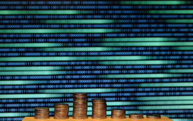 big coin piles in front of out of focus computer screen displayed blue green code matrix. online saving innovation idea.