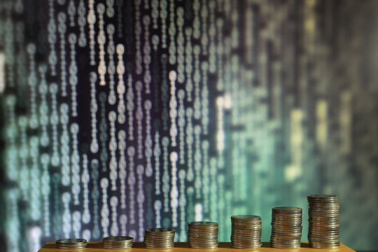 big coin piles in front of out of focus computer screen displayed blue green code matrix. online saving innovation idea.