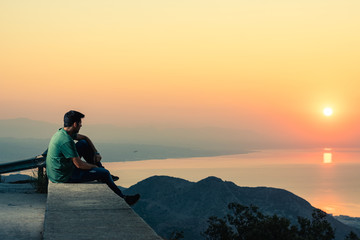 hombre sentado en una montaña mirando el amancer