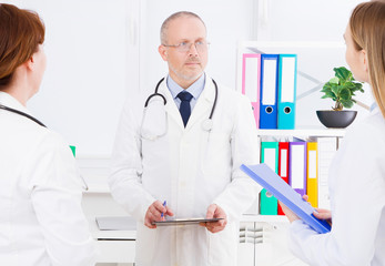 doctor posing in office with medical staff, he is wearing a stethoscope. Quality medicine concept. Man in white uniform. Medical insurance. Selective focus. Copy space