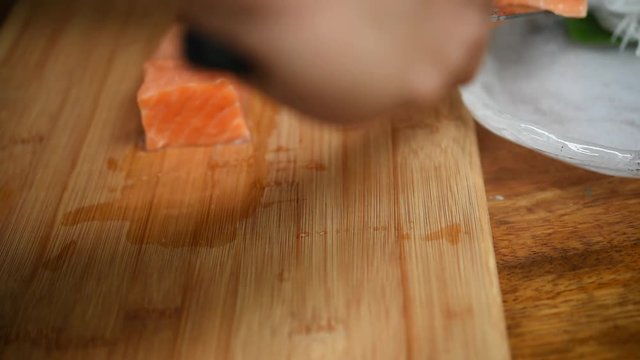Asian chef slice salmon by knife on boad for japanese food delicacy consisting sashimi salmon of very fresh raw salmon fish sliced into thin pieces serving with radish sliced in japanese restaurant