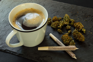 Delicious cup of coffee, a pile of high quality marijuana buds with two cigars of weed ready to...