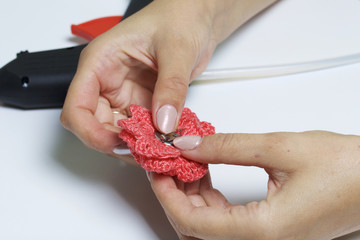 A woman glues a metal hairpin to a knitted brooch in the form of a flower.