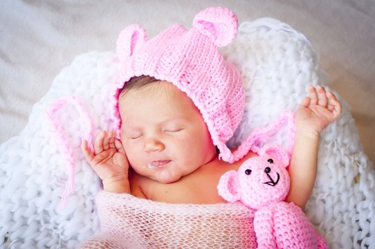 Cute sleeping newborn Caucasian baby girl in a pink hat with ears holding a teddy bear. Sweet infant girl smiling in her sleep. A classical newborn infant photo session. First days of her life concept