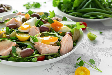 Healthy Nicoise salad with salmon, colourful sweet cherry tomatoes, olives, green beans, cucumber ribbons, soft boiled eggs, water-cress leaves with Mediterranean seasoning