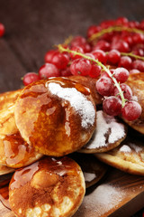 Pancakes or puffertjes with berries and maple syrup on rustic table