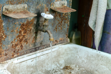 Water flows from a retro plumbing tap into an old sink. Vintage washbasin outdoors.