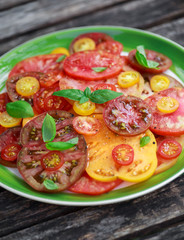 Colorful Tomato Salad with heirloom, pear shaped, beef heart, tigerella, brandywine, cherry, black tomatoes in a green plate. healthy food