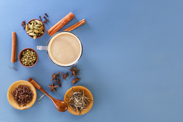 Hot Indian milk tea with spices - cinnamon, cardamom, ginger, cloves, tubby, sweet pepper on a wine background. Top view. Copy space