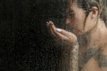 Beautiful woman in the shower washing her face, against a dark background
