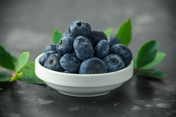 Freshly picked blueberries in white bowl with green leaves. healthy food