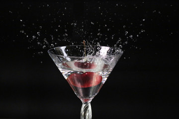 Cherry Fall in to glass of water splash on dark background