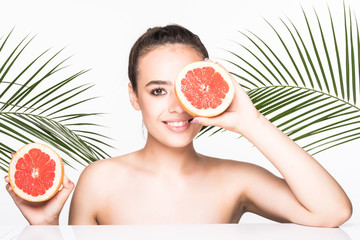 Beauty portrait of a smiling woman perfect skin posing with green leaves and holding sliced orange isolated over white background. Skin care concept.